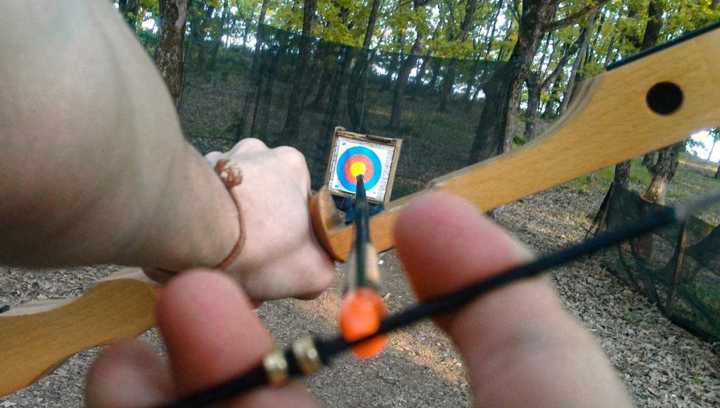 A first-person view of someone holding an arrow and bow with the target in their peripheral vision. The target is in focus whilst the arrow is blurred, showing an example of how to passively aim the bow and arrow.